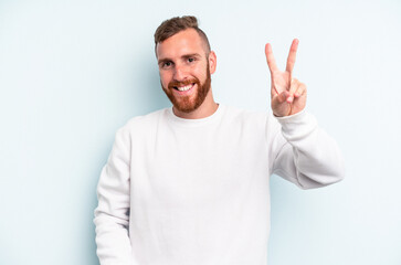 Fototapeta premium Young caucasian man isolated on blue background joyful and carefree showing a peace symbol with fingers.