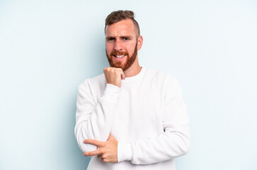 Young caucasian man isolated on blue background smiling happy and confident, touching chin with hand.