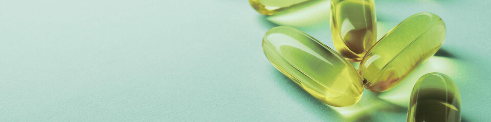 Yellow softgels lie on a green surface. Fish oil. Vitamins and a healthy lifestyle. Banner or header. Softgel closeup. Omega-3 fatty acids capsule. Macro