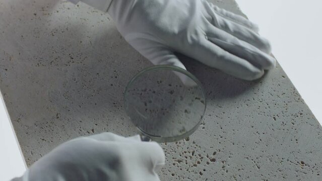 Construction laboratory testing the quality density of natural travertine stone . Worker of laboratory explore stone by loupe . Close up view of hands with gloves . Shot on ARRI Alexa cinema camera