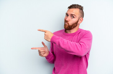 Young caucasian man isolated on blue background shocked pointing with index fingers to a copy space.