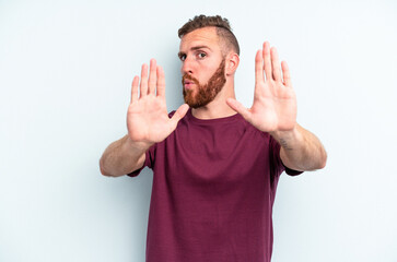 Young caucasian man isolated on blue background standing with outstretched hand showing stop sign,...