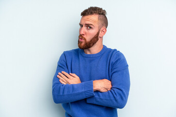 Young caucasian man isolated on blue background unhappy looking in camera with sarcastic expression. - obrazy, fototapety, plakaty