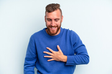 Fototapeta premium Young caucasian man isolated on blue background laughs out loudly keeping hand on chest.