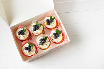 Blueberries cup cakes in delivery box, white wooden board