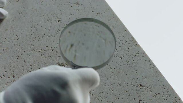 Construction laboratory testing the quality density of natural travertine stone . Worker of laboratory explore stone by loupe . Close up view of hands with gloves . Shot on ARRI Alexa cinema camera