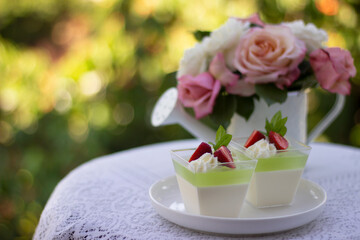 Obraz na płótnie Canvas Panna cotta with lime jelly and fresh strawberry. Dessert in a portion cups on a table in a coffee shop , rose flowers in a pot. Beautiful Desserts.