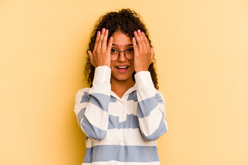 Young Brazilian woman isolated on yellow background having fun covering half of face with palm.