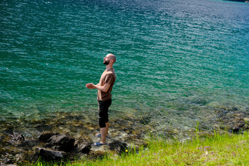 young man of 30 years old gazes intently against backdrop of lake Achensee in Austria, green water, rocks near the shore, concept of vacation by reservoir, resort place tyrol, active lifestyle