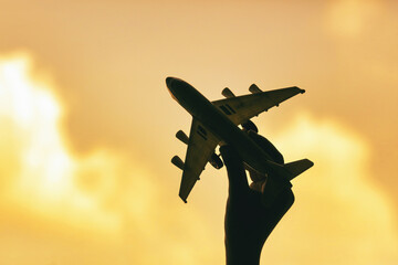 Silhouette of a hand holding a toy plane on a golden sky background
