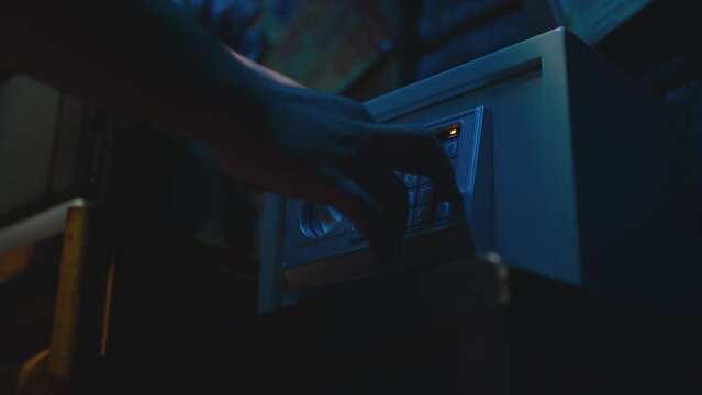 Men's hands opening a safe in the dark room . Man drives the PIN code at the strongbox . Close-up shot of gray safe being opened by a hand entering the correct pin and turning latch . Slow motion .