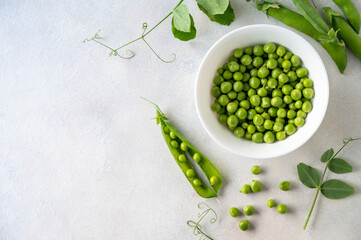 Green fresh peas, snack pea in a white bowl on a neutral grey background. Top view. Summer garden...