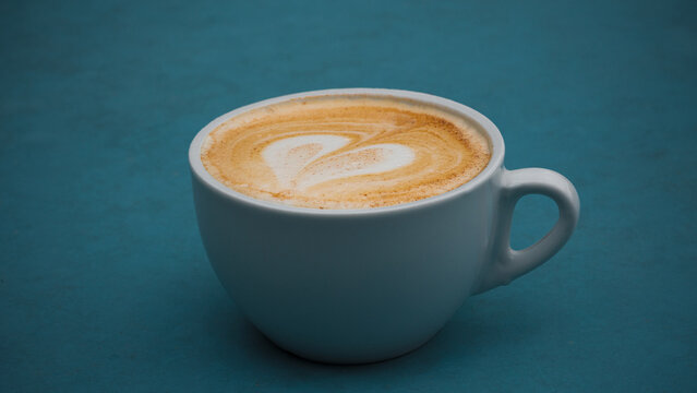 Cup of cappuccino with latte art on a shabby blue surface.