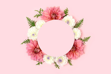 Wreath made of dahlia and green leaves on a pink background. Flower round frame with copyspace.