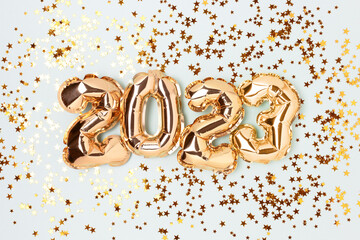 2023 gold foil balloons and confetti on a blue pastel background. Festive concept.