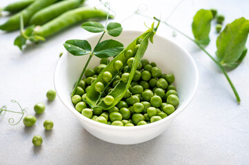 Green fresh peas, snack pea in a white bowl on a neutral grey background. Top view. Summer garden vegetables.