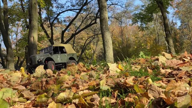 Toy model of soviet military vehicle outdoors. Radio control jeep in khaki colors drives on autumn leaves in a forest.