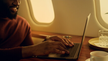 Smiling guy chatting laptop at airplane window closeup. Happy passenger typing