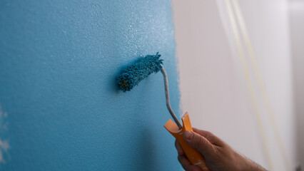 Male decorator painting wall in blue color