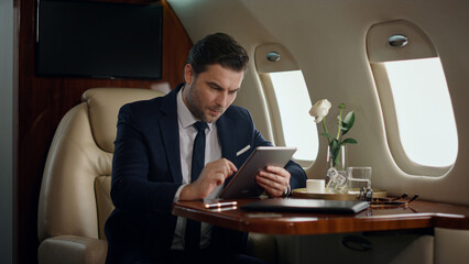 Stressed businessman working tablet in airplane. Professional touch pad screen