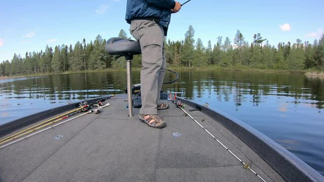 Man fishing artificial lure leans on butt seat to operate trolling motor in the front deck of a bass boat; near docks on Lake Vermilion on a sunny spring day; concepts of fishing and vacation