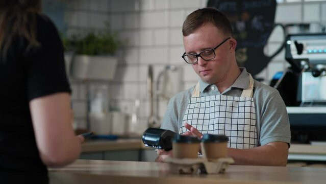 Caucasian man with down syndrome as a waiter accepting contactless payment in the cafe. Shot with RED helium camera in 8K. 