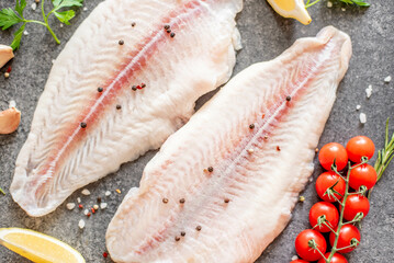 Fresh raw white fish fillet Pangasius with spices and lemon on a stone background.