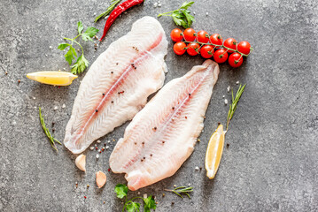 Fresh raw white fish fillet Pangasius with spices and lemon on a stone background.