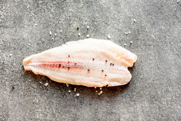 Fresh raw white fish fillet Pangasius with spices and lemon on a stone background.