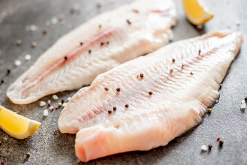 Fresh raw white fish fillet Pangasius with spices and lemon on a stone background.