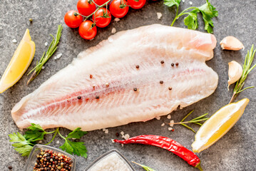 Fresh raw white fish fillet Pangasius with spices and lemon on a stone background.