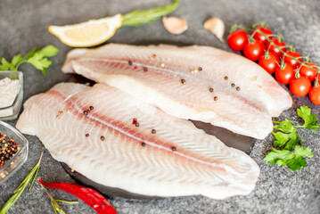 Fresh raw white fish fillet Pangasius with spices and lemon on a stone background.