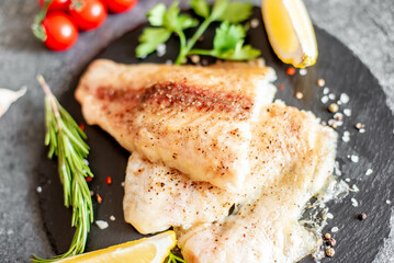 Baked white fish fillet Pangasius with spices and lemon on a stone background - obrazy, fototapety, plakaty