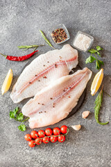 Fresh raw white fish fillet Pangasius with spices and lemon on a stone background.