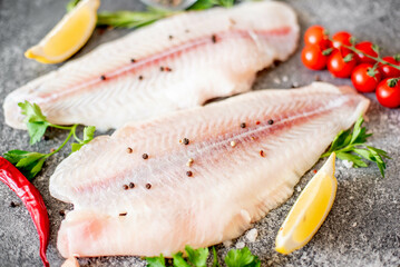 Fresh raw white fish fillet Pangasius with spices and lemon on a stone background.