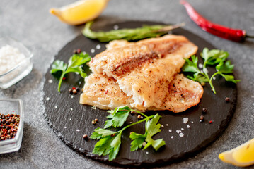 Baked white fish fillet Pangasius with spices and lemon on a stone background - obrazy, fototapety, plakaty