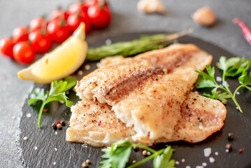 Baked white fish fillet Pangasius with spices and lemon on a stone background
