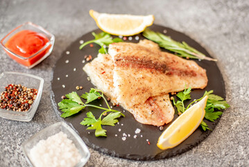 Baked white fish fillet Pangasius with spices and lemon on a stone background