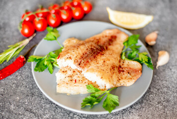 Baked white fish fillet Pangasius with spices and lemon on a stone background