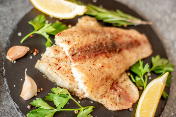 Baked white fish fillet Pangasius with spices and lemon on a stone background