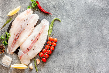 Fresh raw white fish fillet Pangasius with spices and lemon on a stone background with copy space...