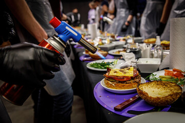 Chef making beef burgers. Melting cheese on a burger bun with a culinary burner for burgers in a restaurant kitchen
