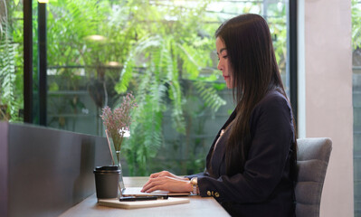 Side view focused businesswoman  working on laptop, typing business email or checking online news.