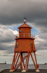 The old, red, wooden Herd Groyne Lighthouse in South Shields, stands out against the cloudy sky
