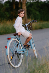Fototapeta na wymiar Romantic portrait of an adorable child. A boy with a bouquet and a bicycle in countryside. Summertime childhood and happiness. Walk in nature. Beautiful sunset. School holidays. purple field. Meadow