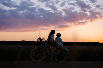 Mom and son are cycling across the field. Family connection joint hobby. Eco-friendly transport bike. Pink field meadow and sunset. Freedom happiness  carelessness. child protection care. Summer time