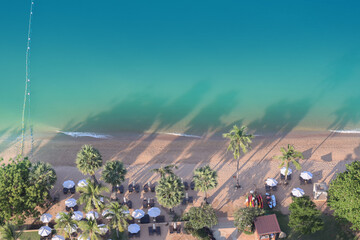 Aerial view from drone show turquoise sea with white wave and resort long beach include palm trees, white umbrella on beautiful tropical summer sunny day for travel and holiday background.
