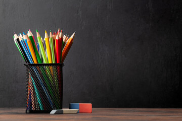 Colorful pencils on wooden table and blackboard