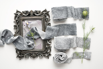 Decorative vintage photo frame, a composition of rolls of different tones of velvet gray ribbon lies on a light background with a small flower