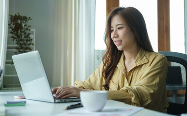 Pretty young female entrepreneur looking at laptop screen, typing business email or checking online news.